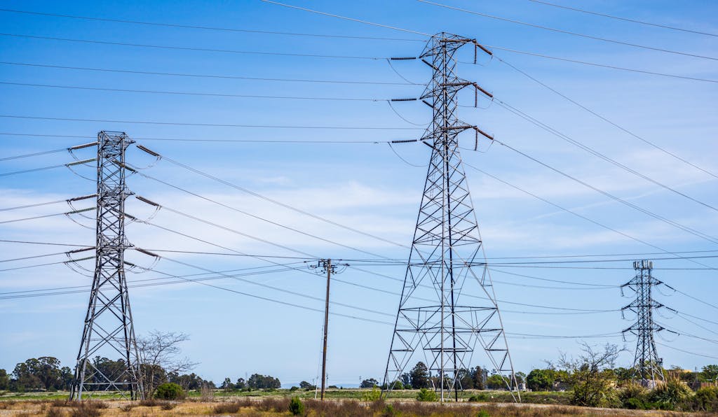 High voltage electric pylons in a field under a clear blue sky demonstrate power transmission infrastructure.